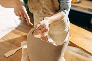 Kadın elleriyle ve özel aletleriyle büyük kahverengi kil çömlek veya vazo yapıyor.