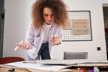 Sloganlarla çalışan kıvırcık kadın atölyedeki dolabın önünde çiziyor.