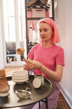 Masada geleneksel kibrit aletleriyle oturan pembe saçlı kadın.