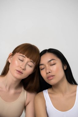 Gri arka planda kapalı gözlerle poz verirken kadınların birbirine bağlanması