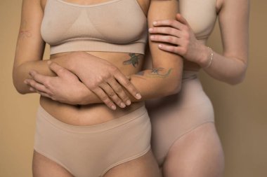 Çilli kız ve dövmeli kız bej arka planda poz verirken kucaklaşıyorlar.