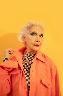 Stüdyoda arka planda sarı duvarlı bir kadın poz veriyor.