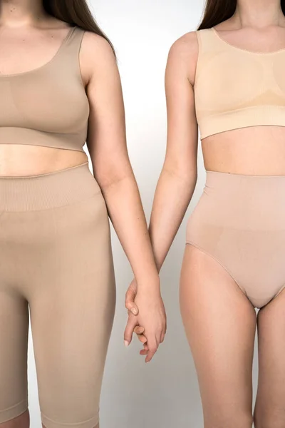 Two girls in underwear with different shapes holding at the hands of each other