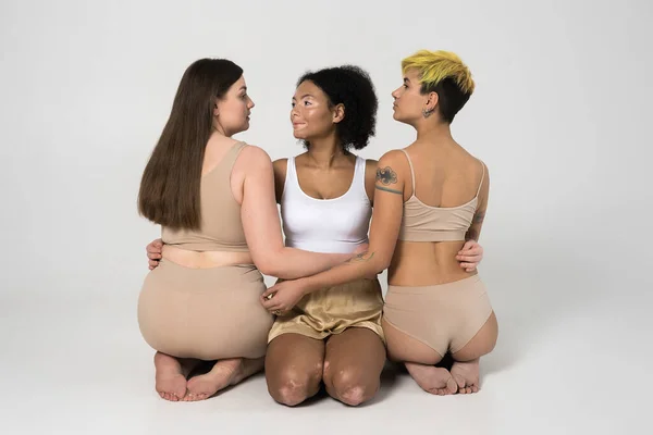 Three diverse girls sitting at the floor and embracing