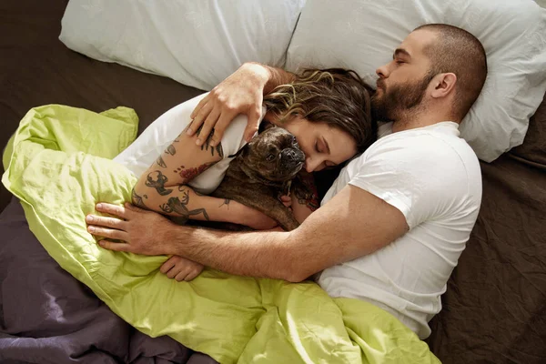 Pareja relajándose en la cama con su cachorro bulldog juguetón mientras abraza — Foto de Stock