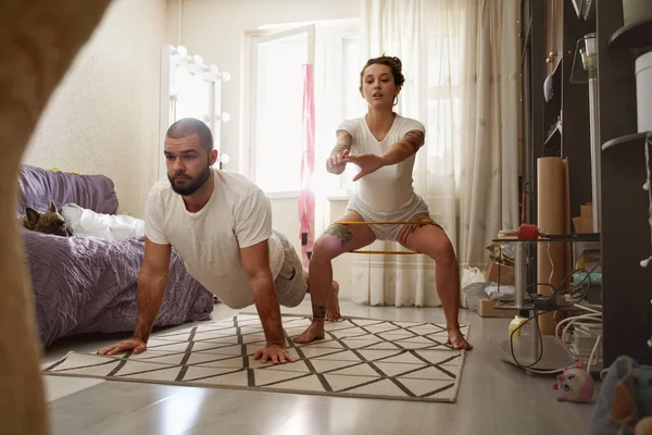 Man op de plank bij het tapijt thuis terwijl zijn vrouw hurken doet — Stockfoto