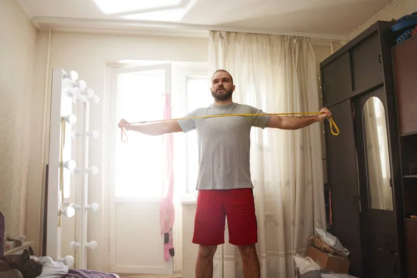 Hombre haciendo ejercicio con una goma mientras hace ejercicio duro en casa — Foto de Stock