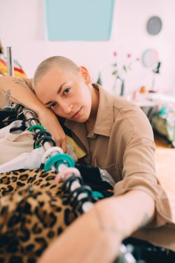 Kısa saçlı kadın askıda yatıyor ve gardırobu incelerken poz veriyor.