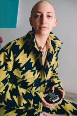 Kalimba müzik aleti tutan ve rahat dairesinde duran ceketli bir kadın.