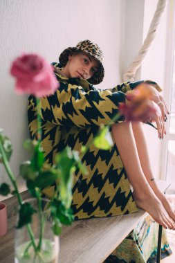 Kafasında leopar desenli panama olan bir kadın evdeki masada oturuyor.