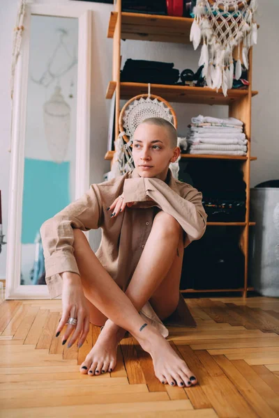 Girl with short hair and tattoos sitting at the floor and looking away — Stock Photo, Image