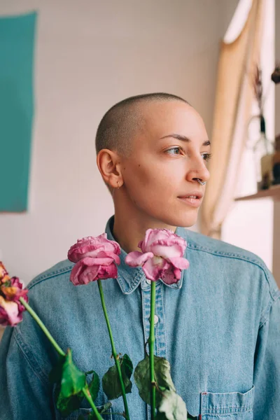 Mulher segurando flores e olhando para a janela enquanto posando em seu apartamento — Fotografia de Stock