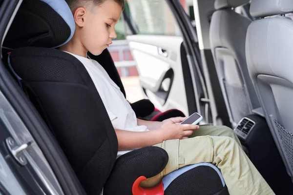 Симпатичный мальчик играет в мобильные игры в машине — стоковое фото