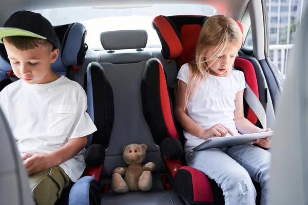 Irmãos bonitos usando gadgets enquanto viajam de carro — Fotografia de Stock