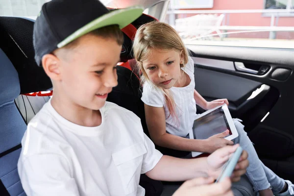 Irmãos alegres brincando com gadgets no carro — Fotografia de Stock