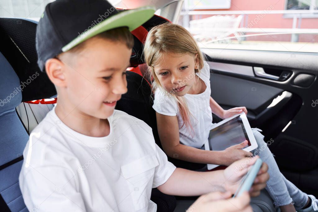 Jolly siblings playing with gadgets in car