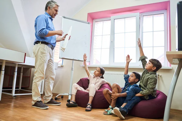 Todos los niños sentados en el aula con las manos levantadas — Foto de Stock