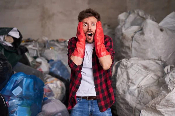 Sorprendido barbudo de pie contra un montón de bolsas llenas de basura — Foto de Stock