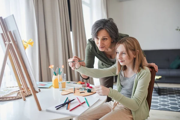 Дівчина дивиться на картину під час малювання біля своєї щасливої бабусі — стокове фото