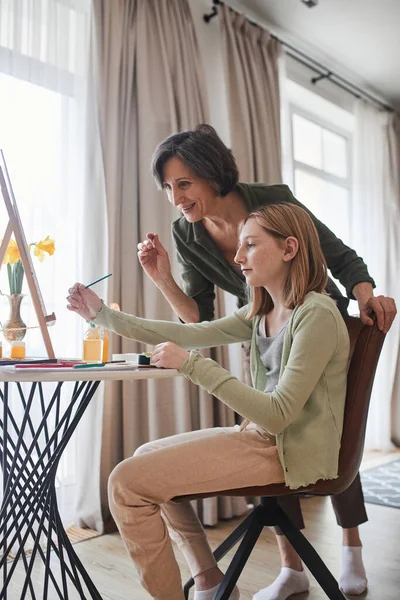 Woman telling something to her granddaughter while helping to drawing to her — Stock Photo, Image