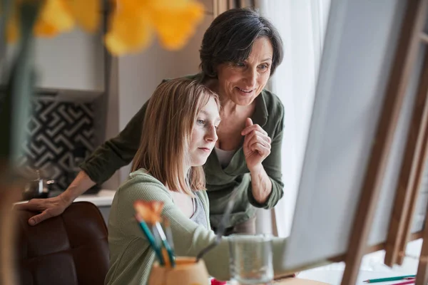 Woman looking with satisfaction at the drawing of her blonde granddaughter