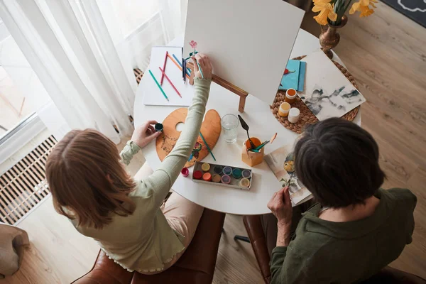 Kid creating with paints while her grandmother sitting near and drawing — Stock fotografie
