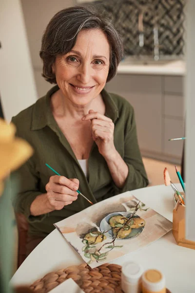 Elderly woman smiling toothy to the camera while drawing fruits — Stockfoto