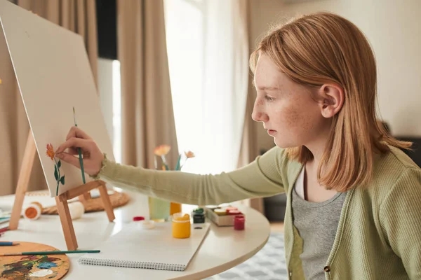 Beautiful female kid artist paints on canvas with colors in her living room — Stock fotografie