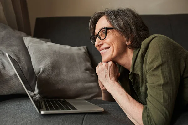 Жінка в окулярах дивиться на екран ноутбука під час спілкування з друзями — стокове фото