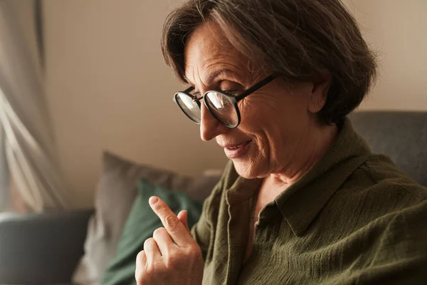Жінка в окулярах дивиться щось на її ноутбук, сидячи на дивані — стокове фото