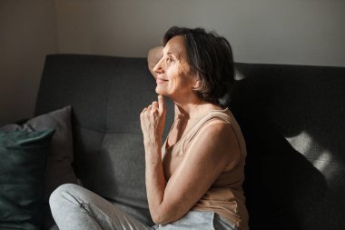 Kanepede oturan ve pencereye bakan kadın gülümsedi.