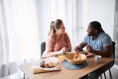 Adam masada oturmuş salata yerken karısıyla konuşuyor.
