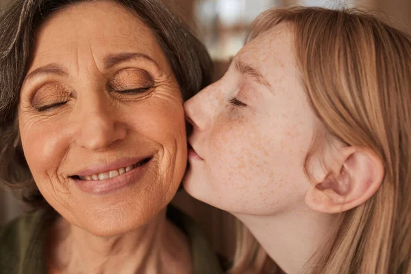 Freckled girl kissing with tenderness her lovely grandmother — Photo