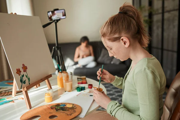 Girl artist sitting in front of the smartphone at the tripod in her living room — Stock fotografie