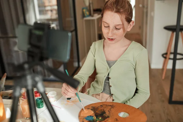 Ginger girl drawing with acrylic paints while broadcasting for her blog about art — Stock fotografie