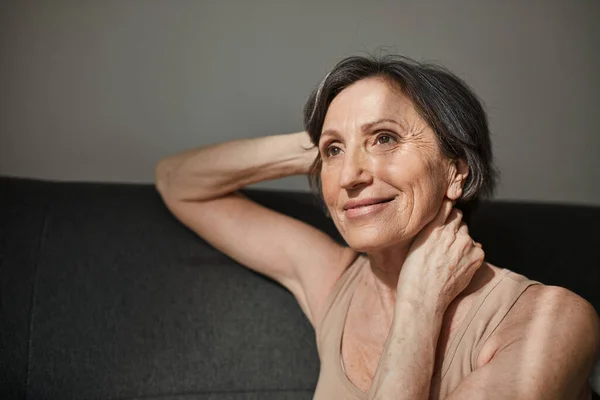 Woman sitting at the sofa and looking at the window with pleasure smile — Stock Photo, Image