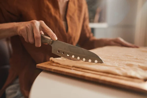 Woman chopping with the knife fresh dough while baking bagels at the kitchen — Stockfoto