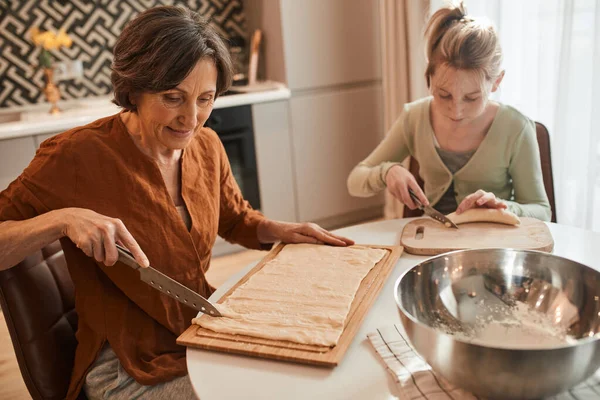 Woman chopping with the knife fresh dough while baking bagels with her granddaughter — Stockfoto