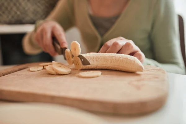 Young girl chopping with the knife fresh banana while baking bagels at the kitchen — Stockfoto