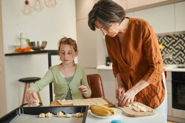 Grandmother with her granddaughter cooking dish together, while preparing fresh bagels