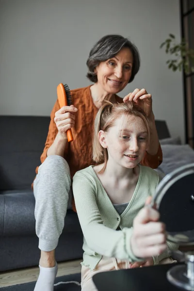 Mujer sonriendo y cepillando el cabello para su pecosa nieta en la sala de estar — Foto de Stock