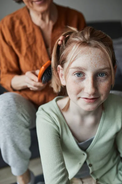 Chica sonriendo y mirando a la cámara mientras su abuela preparando el peinado — Foto de Stock