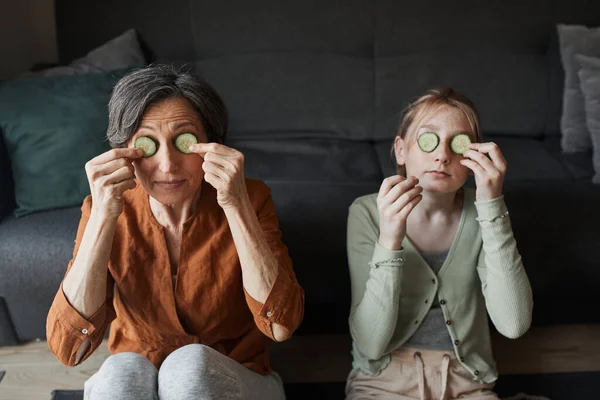 Chica y su abuela poner rebanada de pepino en los ojos, mientras que el cuidado de su piel —  Fotos de Stock