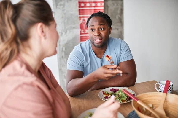 남자가 식탁에 앉아서 샐러드를 먹으면서 아내와 이야기하는 모습 — 스톡 사진