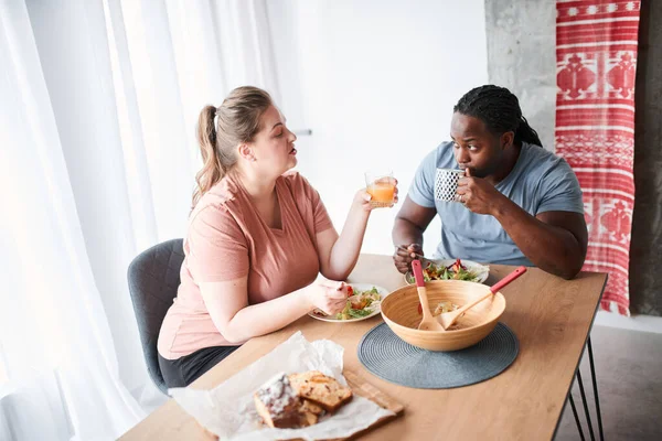 Couple talking during breakfast while sitting at the kitchen and eating salad