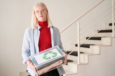Giysilerle dolu geri dönüşüm sembollü plastik şeffaf kutu tutan adam.