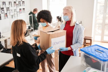 Adam ve meslektaşı koruyucu maskeler takıyor. Kıyafet bağışlarıyla dolu kutuları alıyorlar.