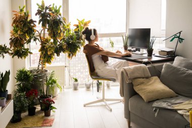 Masada oturan kadın bilgisayar ekranına bakıyor ve müzik dinliyor.