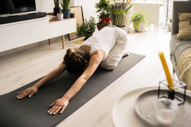 Spor kıyafetli bir kadın yerde otururken çocuk pozu veriyor.