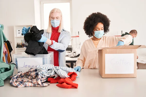 Mulher e seu colega albino masculino vestindo máscaras protetoras examinando roupas — Fotografia de Stock